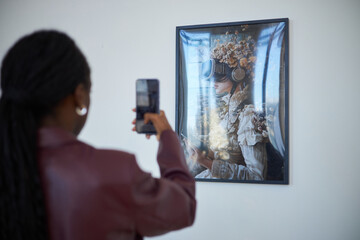 Person capturing image of intricate artwork at gallery using smartphone camera. Painting features...