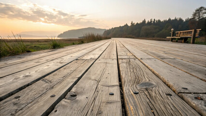 Aged wooden deck extends into distance near body of water during sunset, with bench on side and scenic landscape in background.