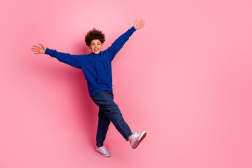 Cute young boy in blue hoodie posing playfully with open arms against vibrant pink background