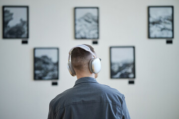 Person wearing headphones viewing an art installation with photographs on wall. Headphones indicating an immersive guided experience with art exhibitions being observed