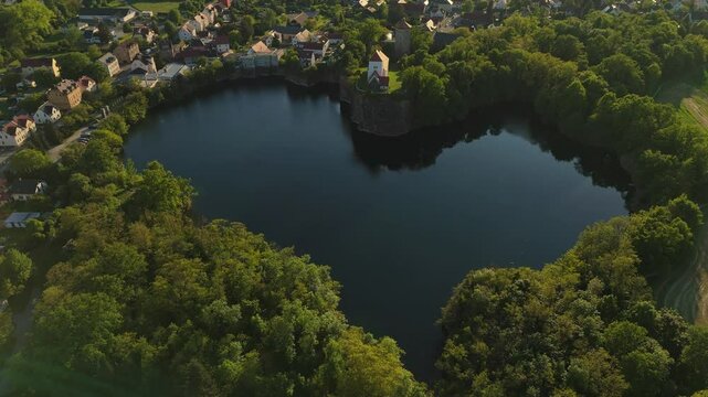 Cinematic orbit of the Wehrkirche Beucha above a heart-shaped quarry lake in Saxony, Germany. Captured during golden hour. Aerial view of village, water, trees and church on a cliff.