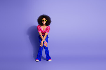 Young fashionable woman posing joyfully in vibrant clothing against a bright purple backdrop showcasing retro style
