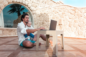 dad and his little son with a laptop are resting and working as a freelancer on vacation
