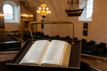 An open holy book rests at the front, gazing out over the church, where the chandelier glimmers above the nave