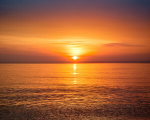Fototapeta premium Orange and golden light reflects on the water as the beautiful sun dips below the ocean horizon