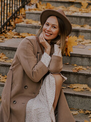 Beautiful blonde young woman in hat and coat sitting on the stairs in the autumn park.
