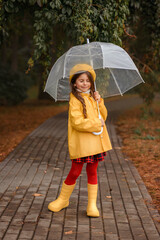 little girl in yellow raincoat and yellow jacket red plaid skirt on the street in autumn