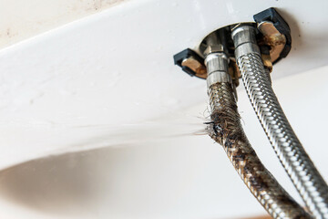 The faucet connection hoses, one of which is burst and water is coming out of it under pressure