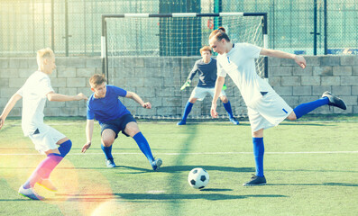 Game moments of football match between two teams of teenagers in white and blue shirts