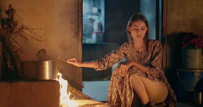 Indian gen z young villager woman preparing food using traditional earthen mud stove indoor house asian teen age female cooking on open fire flam inside kitchen home