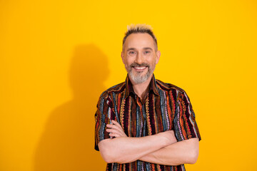 Cheerful middle aged man with dyed blond hair and a trendy print shirt on a vibrant yellow background exuding joy and style