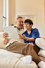 Obraz premium Happy couple sharing a moment at home while enjoying a tablet together