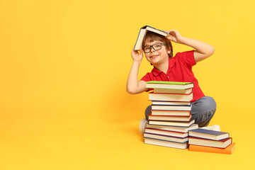 Boy with many different books on orange background. Space for text