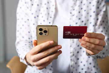 Woman with credit card and smartphone paying online on blurred background, closeup