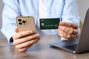Woman with credit card, smartphone and laptop paying online at wooden table, closeup