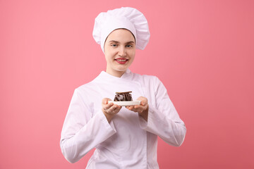 Confectioner in uniform holding delicious chocolate dessert on pink background