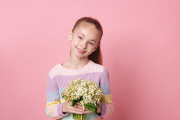 Girl with bouquet of beautiful lily-of-the-valley flowers on light pink background