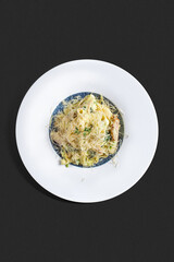 Top-view photograph: a plate of creamy pasta with chicken fillet, green onions, and a generous amount of grated cheese, garnished with a small herb sprig. 