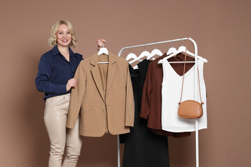 Smiling fashion stylist and rack with clothes on beige background