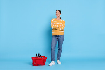 Smiling woman and shopping basket on light blue background