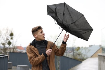 Man with broken umbrella fighting wind under rain outdoors