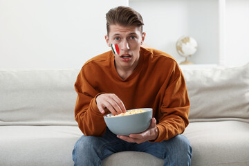 Sports fan eating popcorn while watching game on sofa indoors