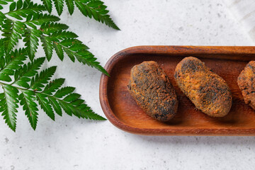 Delicious fried squid ink croquettes resting on wooden tray next to fern