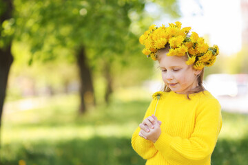 Cute little girl with beautiful flower wearing wreath of dandelions in park, space for text