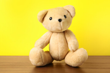 Cute teddy bear on wooden table against yellow background