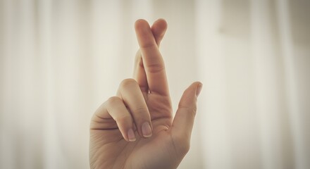 Naklejka premium Fingers crossed, Close-up of a left hand with crossed fingers against a plain background, conveying luck, trust, or anticipation