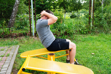 Man doing sit-ups outdoors on yellow fitness equipment. Healthy lifestyle, workout.