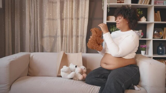 Happy moments of pregnancy and motherhood, african woman unpacking bag with toys . Goods for children, future mother talking teddy bear from paper bag after shopping, prepare to childbirth, parenting