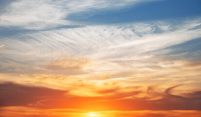 A radiant sunset with vivid orange and golden hues blending into delicate wisps of clouds under a deepening sky.
