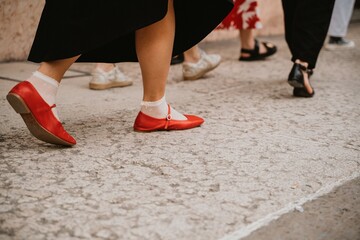 A group of people walking on a city street with focus on their shoes. Red shoes paired with white...