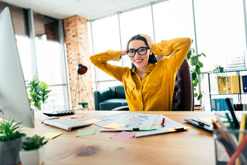Smiling young businesswoman at a cluttered modern workspace enjoying her day with confidence and...