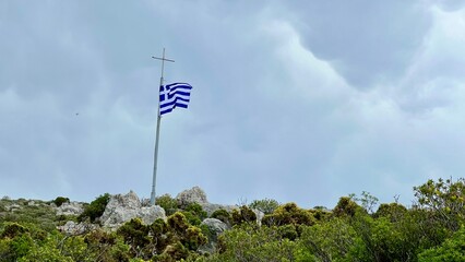 Obraz premium Greek flag waving in the wind against dramatic sky, Kastellorizo island, Greece, national symbol, Mediterranean atmosphere, travel destination, patriotic scene, tourism, culture, copy space 