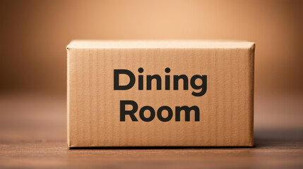 Cardboard box labeled Dining Room placed on wooden surface with blurred background, suggesting storage or moving