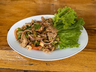 Spicy minced pork salad (Larb Moo), a popular Thai northeastern dish, served on a white plate with fresh vegetables on a wooden table.