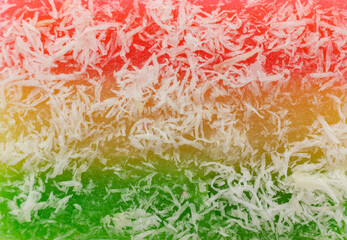 A close-up textures of Indonesian Sentiling cake or called Ongol ongol, featuring red, yellow, and green hues. The cake's surface is generously coated with shredded coconut.