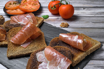 Rustic toast with Spanish ham, cherry tomatoes, and walnuts on a wooden surface. Traditional Mediterranean breakfast concept
