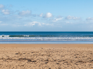 Gentle waves rolling onto sandy beach under blue sky