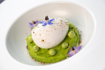A fresh pea puree is beautifully plated, featuring a poached egg at the center and adorned with borage flowers. The dish showcases vibrant colors and textures, perfect for any spring menu.