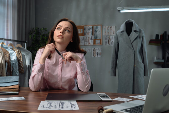 Young adult businesswoman spending time in office, woman fashion designer thinking getting inspiration, working on laptop using graphic tablet, creating new clothing models.