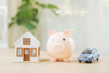 House and car models next to piggy bank signify saving for property and automobile ownership....