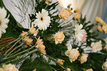 White gerbera daisies and soft peach roses are arranged with lush green foliage