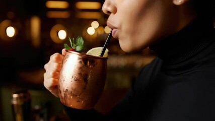 Woman sipping cocktail from copper mug garnished with mint and lemon - Powered by Adobe