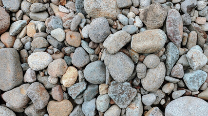 River rock background. A collection of river rocks with varying shapes, sizes and colors. Photo of rocks on the riverbank.