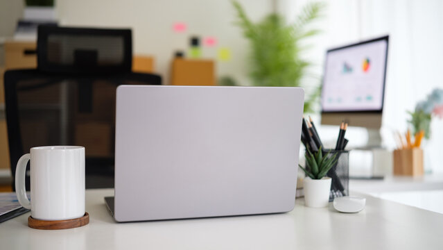 Minimalist modern workspace with laptop, coffee mug, and office supplies on white desk in home office.