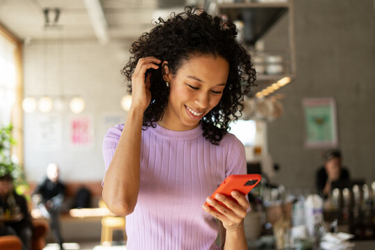 Young woman using mobile phone, touching her hair and smiling in a cafe