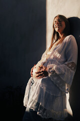 Happy pregnant woman touching her belly, enjoying the wait of her baby, fair skin and a calm smile on her face